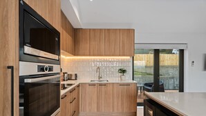 Une cuisine moderne avec des meubles en bois, un four encastré et une grande fenêtre donnant sur un jardin.