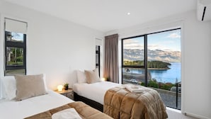 Une chambre d’hôtel avec deux lits, une grande fenêtre donnant sur la montagne et le lac, et une petite table de chevet avec une lampe.