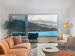 Un salon moderne doté d’une grande porte-fenêtre coulissante donnant sur un balcon avec vue sur les montagnes.