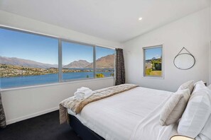 A bedroom with a large window, a bed, a mirror, and a view of mountains and water. - Epic Views and Deck | Spacious Queenstown Home (Queenstown)