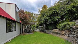 Un jardin bien entretenu avec une terrasse, un mur en pierre et une pelouse verdoyante.