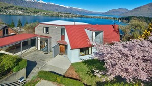 Une maison moderne avec un toit rouge, une véranda en verre et une vue sur un lac et des montagnes.