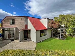 A two-story house with a red roof, a covered patio, and a well-maintained lawn.