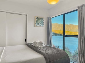 A room with a bed, a window with a view of a body of water and mountains, and a painting on the wall.