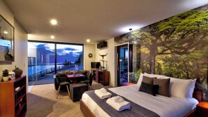 Une chambre d’hôtel moderne avec un grand lit, un bureau et une vue sur les montagnes, visible à travers la porte vitrée.
