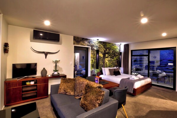A modern hotel room with a large bed, a sofa, a TV, and a large window with a view of the outdoors.