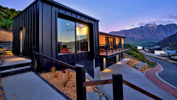 Un bâtiment moderne à deux étages, doté de grandes fenêtres, d’un balcon et offrant une vue sur les montagnes.