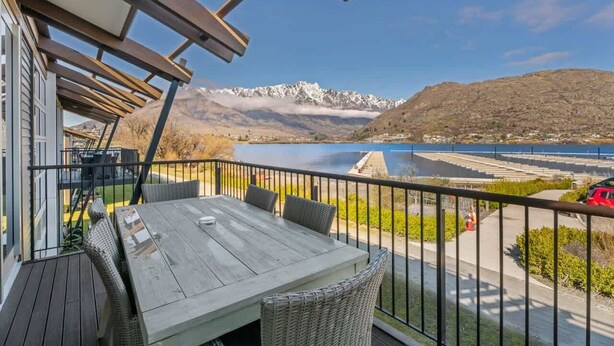 Ein Balkon mit Tisch und Stühlen, mit Blick auf einen See und Berge.