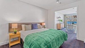 Ein Hotelzimmer mit Bett, Nachttischen, einem Schreibtisch und Meerblick.