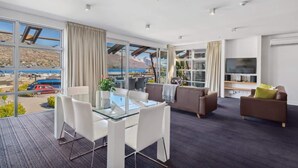 Ein modernes Wohnzimmer mit einem Glastisch, weißen Stühlen, einem braunen Sofa und einem Fernseher.