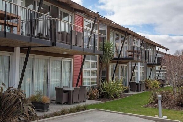A multi-story residential building with balconies, a small outdoor seating area, and a well-maintained lawn.