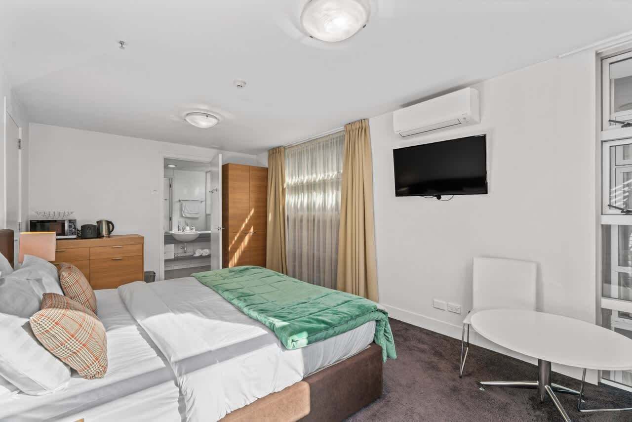 Une chambre d’hôtel avec un lit, un bureau, une chaise, une télévision et une salle de bain visible à travers une porte ouverte.