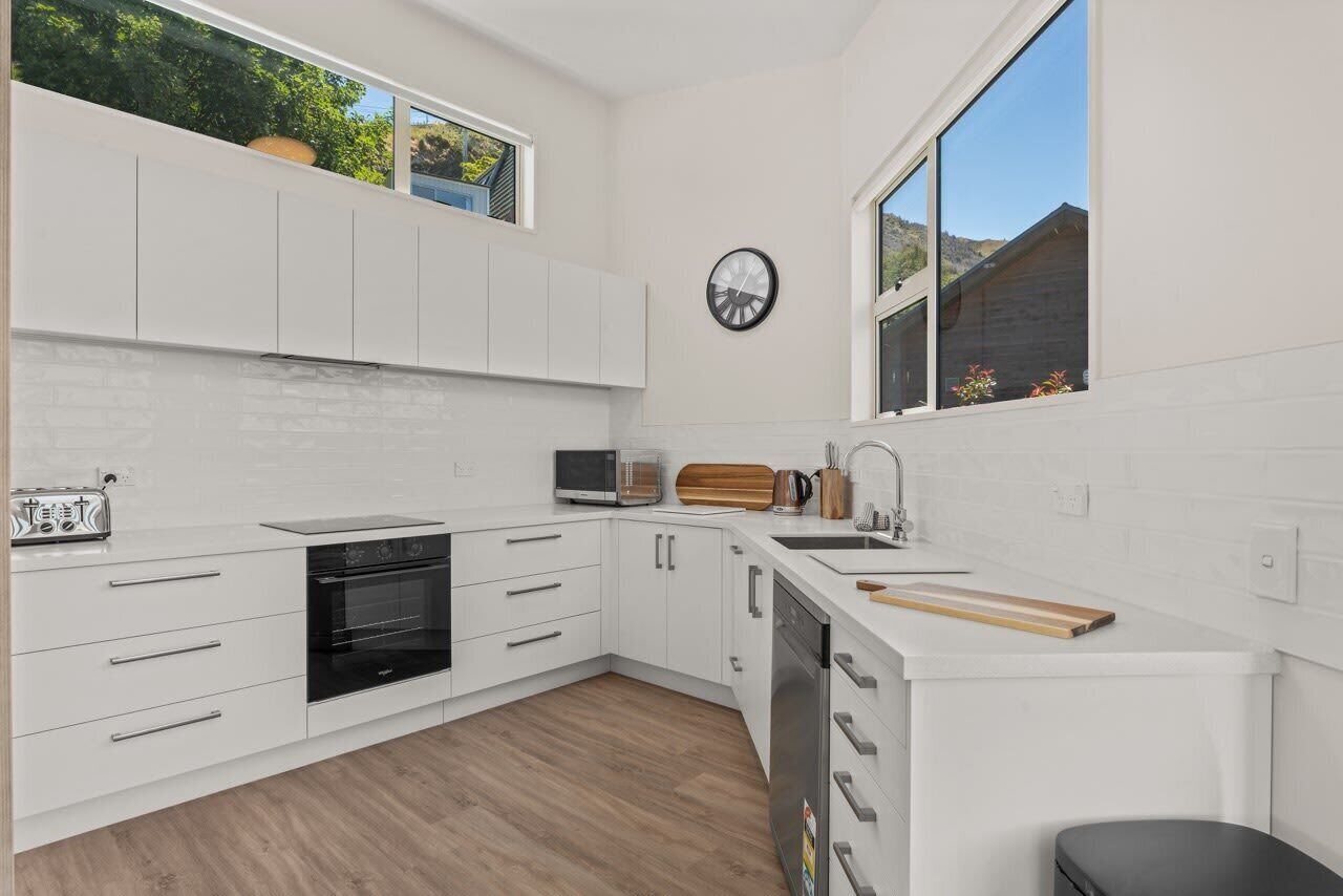 A modern kitchen with white cabinetry, a built-in oven, a microwave, a sink, and a window with a view of greenery.