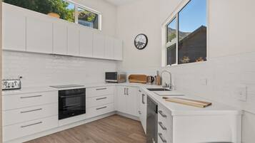 A modern kitchen with white cabinetry, a built-in oven, a microwave, a sink, and a window with a view of greenery.