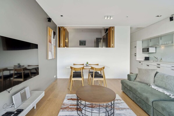 Una sala de estar moderna con un sofá, una mesa de comedor con sillas, un televisor y una cocina con microondas.