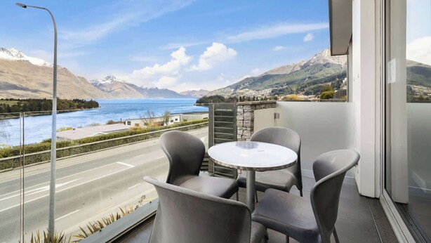 A balcony with a table and chairs overlooking a road and a body of water with mountains in the background. - Lakeview Premium 2 Bed Apartment Pounamu 203 (Queenstown)
