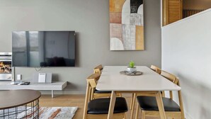 A modern living room with a flat-screen TV, a painting, and a dining area with a table and chairs. - Lakeview Premium 2 Bed Apartment Pounamu 203 (Queenstown)