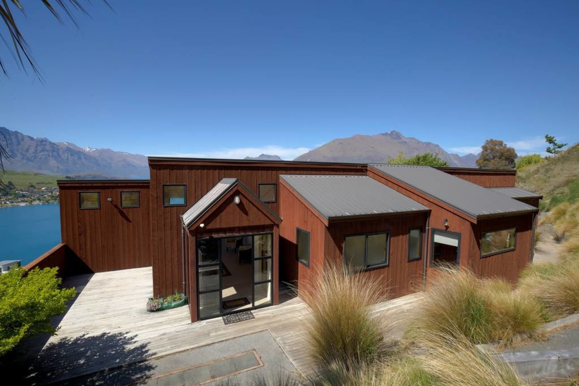 Una casa moderna de madera con amplios ventanales y una terraza con vistas a un lago y montañas.