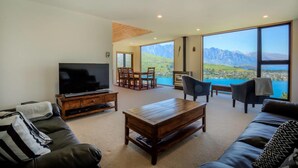 A modern living room with a large TV, comfortable seating, a wooden coffee table, and a scenic mountain view through large windows.