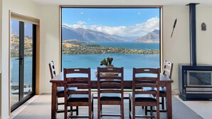 A dining area with a table and chairs, a fireplace, and a large window with a view of a lake and mountains.