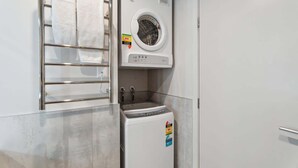 A compact laundry room with a built-in washer and dryer, a metal towel rack, and a small sink. - Studio Getaway, Remarkables Views, Frankton (Queenstown)