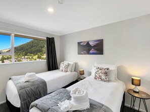 Habitación de hotel con dos camas, un cuadro y vistas a un paisaje montañoso, además de una ventana con cortinas.