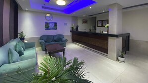A modern reception area with a reception desk, two sofas, a small table, and potted plants.
