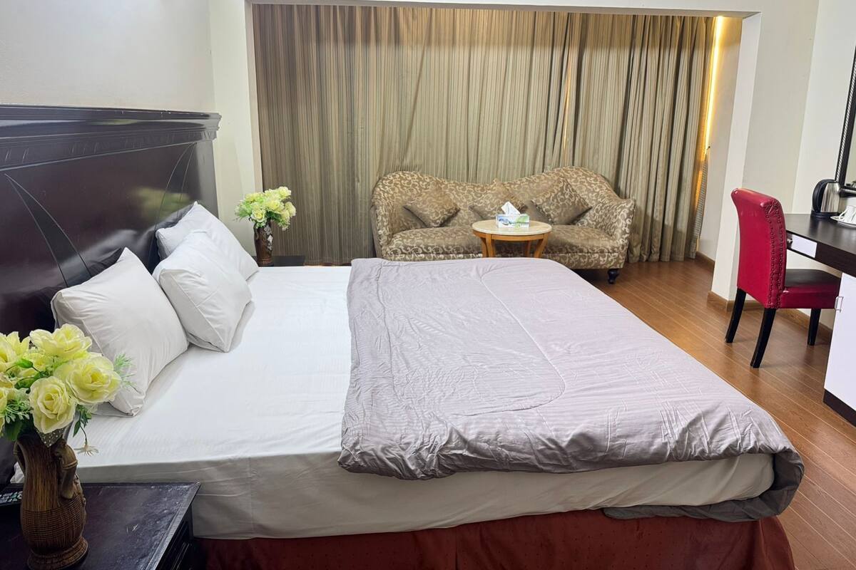 A hotel room with a large bed, a sofa, a desk, and a chair.