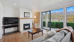 A modern living room with a flat-screen TV, fireplace, comfortable seating, and a large window offering a mountain view.
