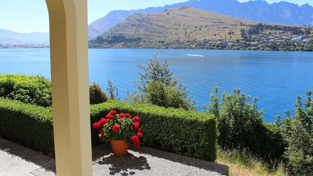 A view of a lake with mountains in the background and a potted plant with red flowers in the foreground.