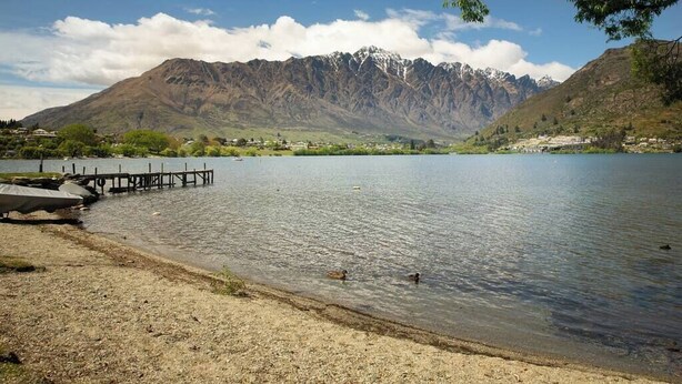 A lake with mountains in the background, a dock, and a few ducks swimming.