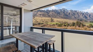 A balcony with a wooden table and chairs, overlooking a mountainous landscape. - Modern apartment with fantastic mountain views! (Queenstown)