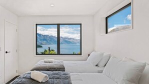 A hotel room with two beds, a large window with a mountain and lake view, and a small window above the bed.