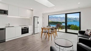 A modern kitchen with white cabinetry, a dining area with a table and chairs, and a large window offering a mountain view.