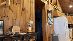 Interior de madera con una escalera de madera, una zona de cocina con refrigerador y una pared de madera con un cartel.