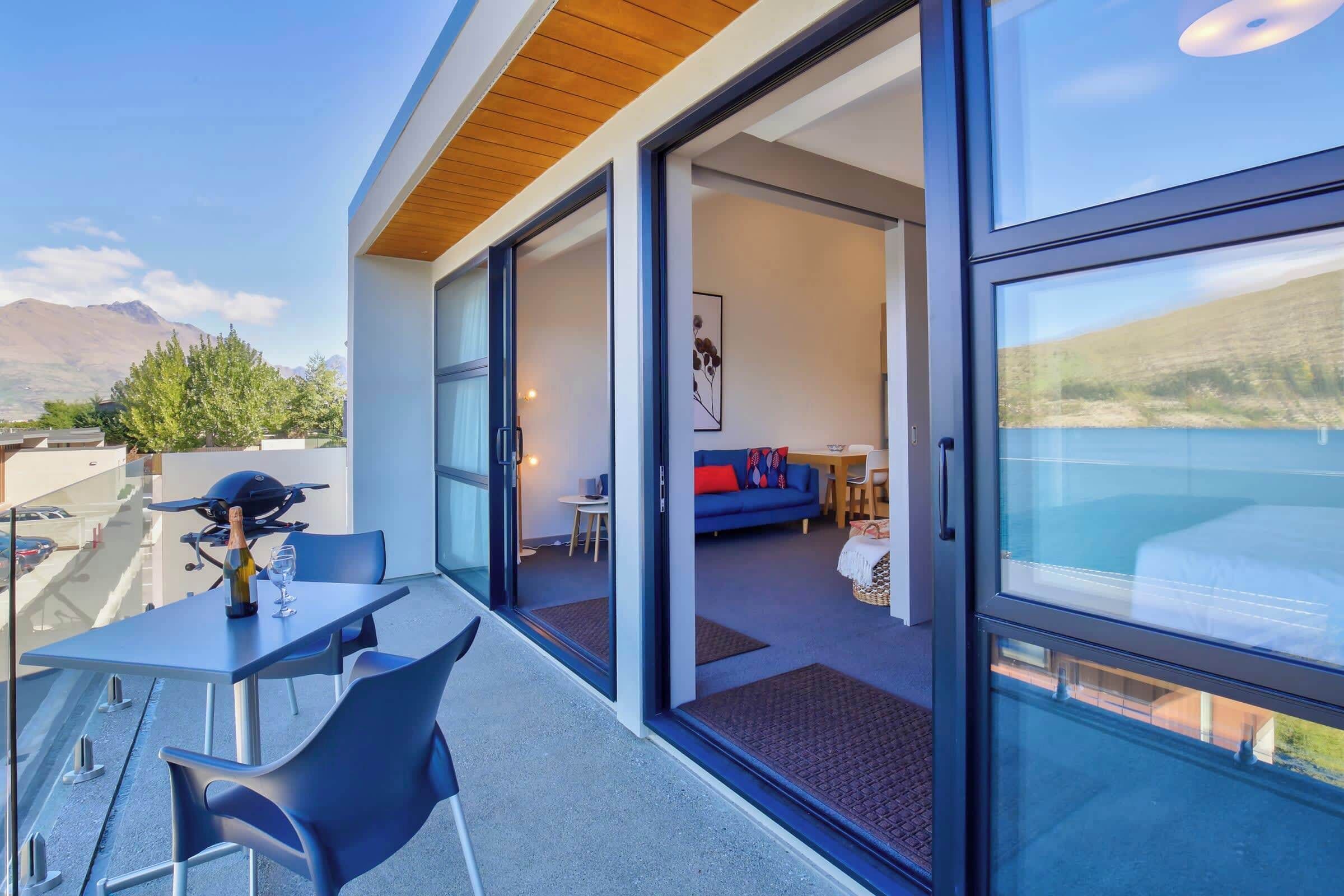 A modern outdoor balcony with a dining table and chairs, a grill, and a view of the mountains.