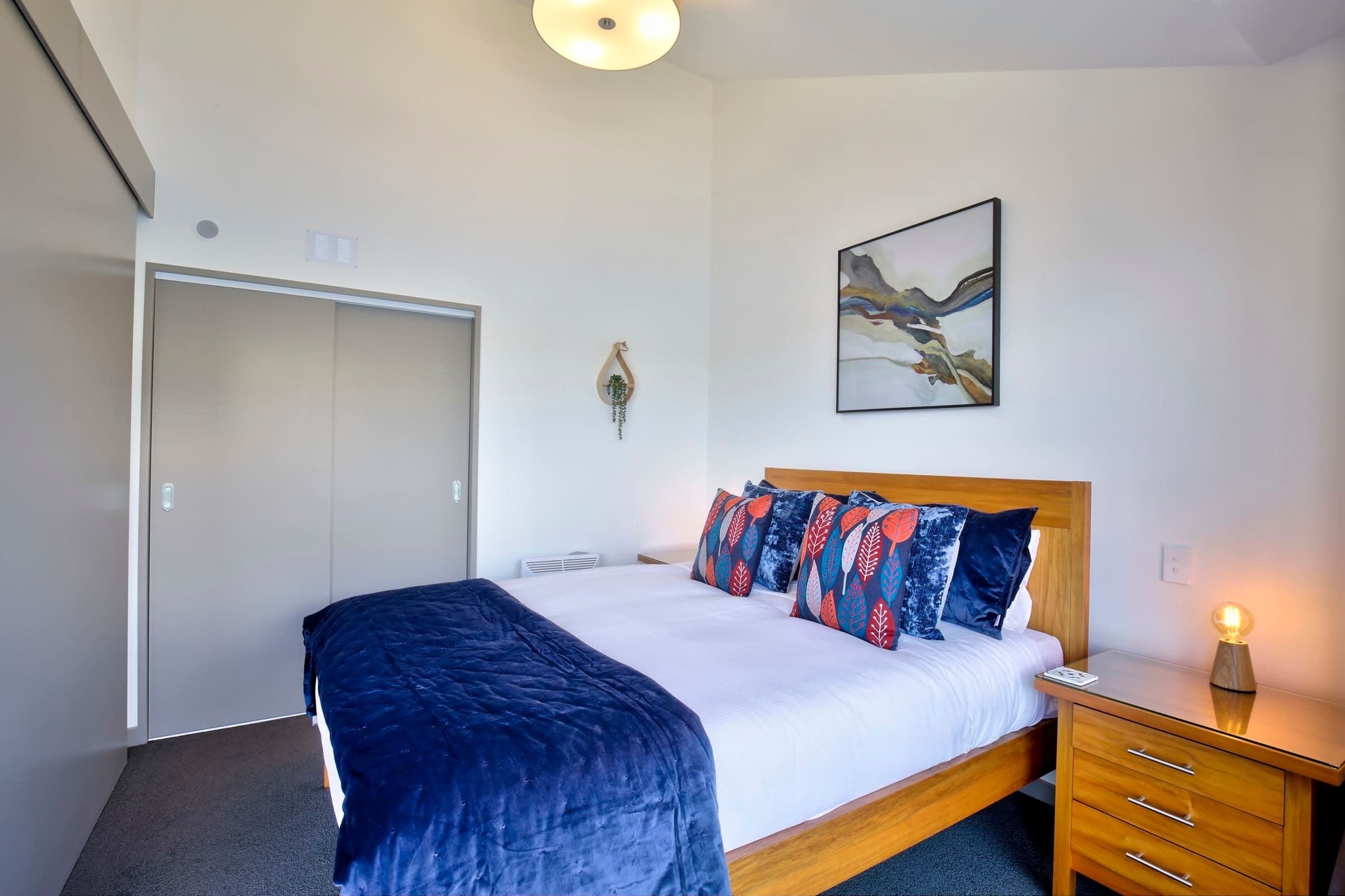Une chambre d’hôtel avec un lit, une table de chevet avec une lampe, une armoire et un tableau au mur.