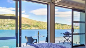 Una camera da letto con un'ampia finestra vista su un lago e delle colline.