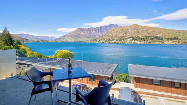 Una terrazza con tavolo e sedie che si affaccia su un lago e montagne.