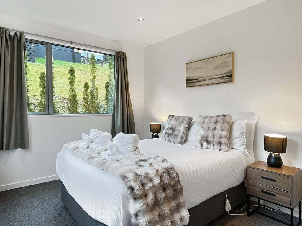 A bedroom with a large bed, two bedside tables, a window with curtains, and a painting on the wall.