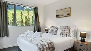 A bedroom with a large bed, two bedside tables, a window with curtains, and a painting on the wall.