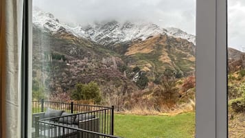 A view from a window with a balcony, overlooking snow-capped mountains and a grassy landscape.