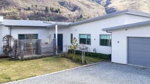 Ein modernes, zweistöckiges Haus mit weißer Fassade, einem Schotterweg und einem eingezäunten Garten.