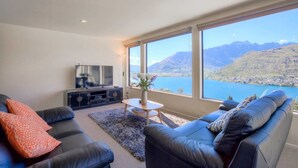 A modern living room with a large window offering a scenic view of mountains and a lake.