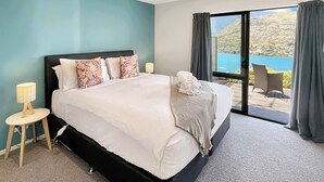 A modern hotel room with a large bed, a small bedside table with a lamp, and a view of a scenic landscape through a large window.