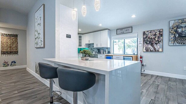 A modern kitchen with a white island, bar stools, pendant lights, and artwork on the walls. - Luxury & Spacious/Large pool/BBQ/Game room/Pool (Miami)