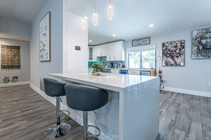 A modern kitchen with a white island, bar stools, pendant lights, and artwork on the walls. - Luxury & Spacious/Large pool/BBQ/Game room/Pool (Miami)