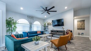 A modern living room with a teal sofa, a wooden coffee table, and a ceiling fan. - Luxury & Spacious/Large pool/BBQ/Game room/Pool (Miami)