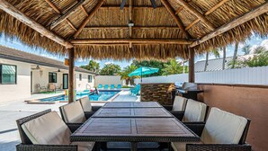 A covered outdoor dining area with wicker furniture and a pool in the background. - Luxury & Spacious/Large pool/BBQ/Game room/Pool (Miami)