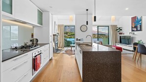 A modern kitchen with a central island, a dining area with a view, and a living space with a TV and seating.